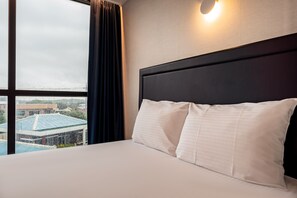A hotel room with a large bed, a window with curtains, and a view of buildings outside.