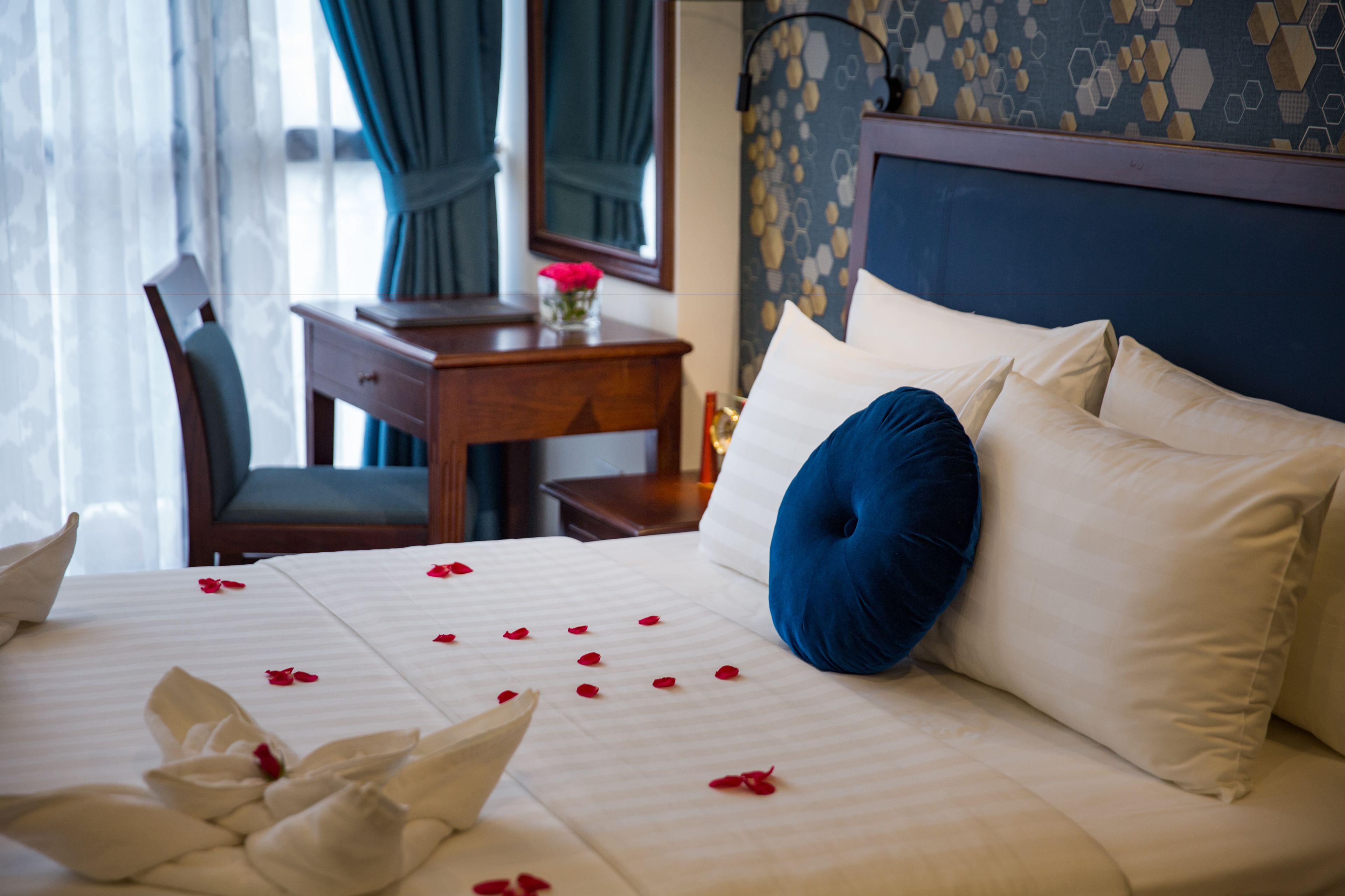 A hotel room with a neatly made bed, a desk with a chair, and a decorative mirror.