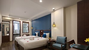 A hotel room with two beds, a desk with a laptop, a chair, and a small table with a vase of flowers. - Holiday Emerald Hotel (Hanoi)