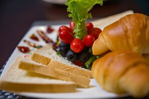 A plate with a croissant, slices of bread, cherry tomatoes, and a leafy vegetable. - Holiday Emerald Hotel (Hanoi)