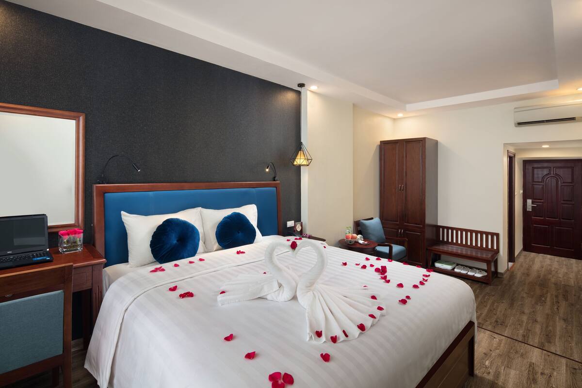 Une chambre d’hôtel avec un lit bien fait, un bureau avec un ordinateur portable, une chaise, une armoire et un banc.