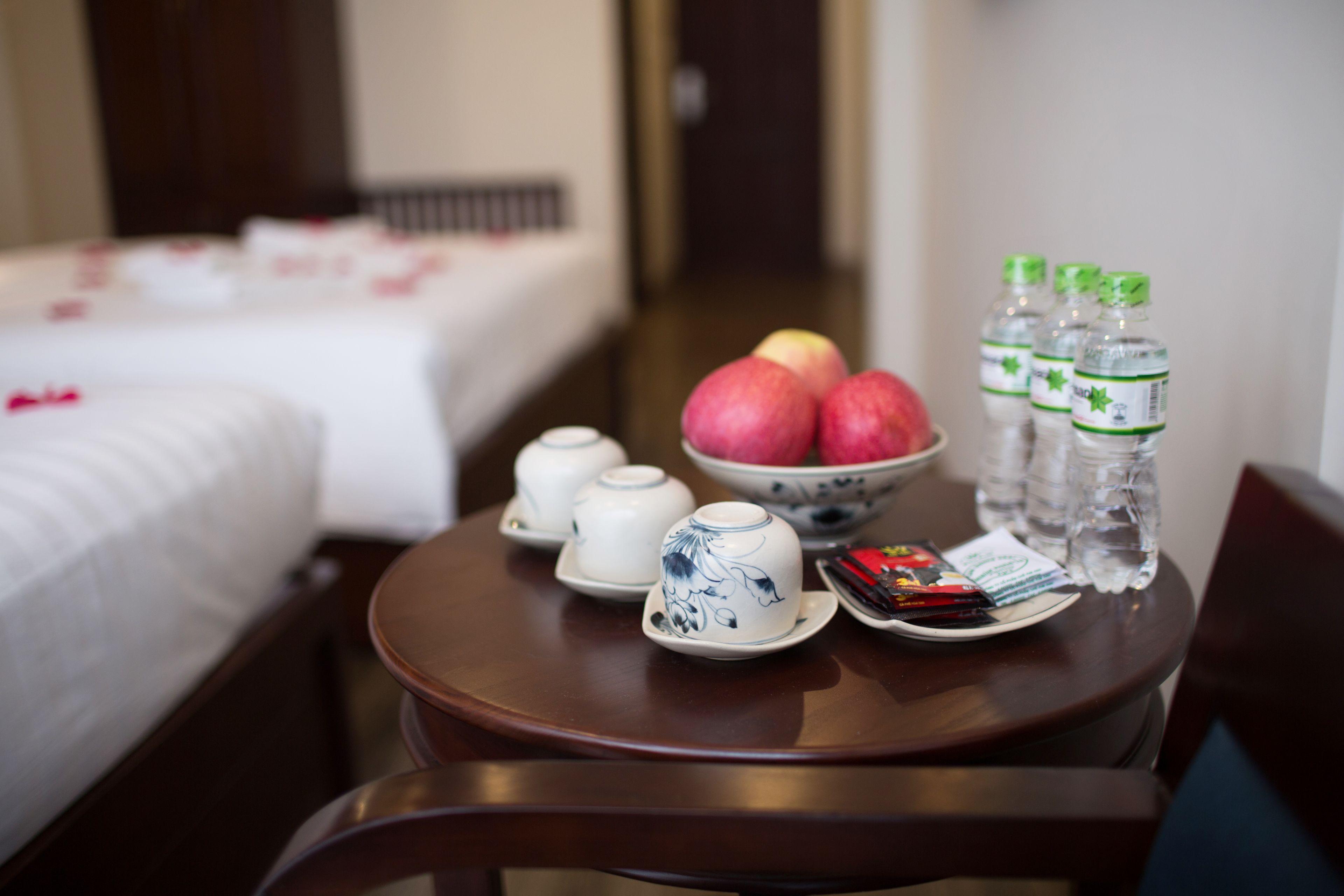 Ein Hotelzimmer mit einem ordentlich bezogenen Bett, einem Esstisch mit Teekannen, Tassen, Äpfeln und Flaschenwasser.