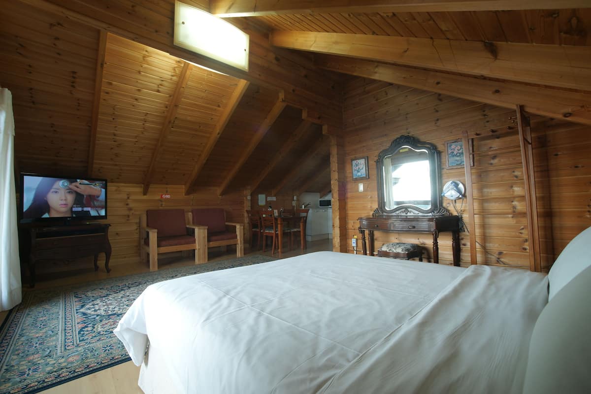 Ein Schlafzimmer einer Holzhütte mit einem großen Bett, einem Fernseher, einem Schreibtisch und einem Sessel.