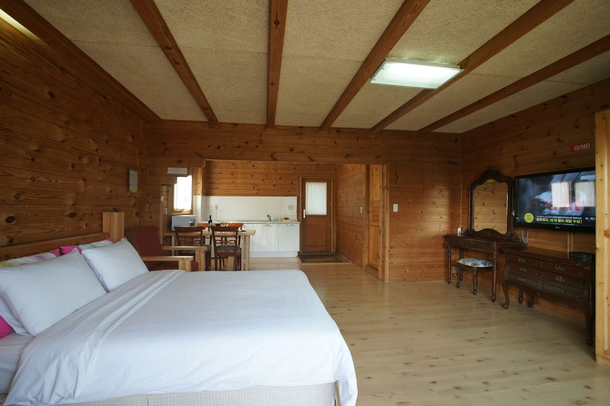 Ein Holzhütten-Zimmer mit einem Bett, einem Schreibtisch, einem Sessel, einem Fernseher und einem kleinen Tisch.