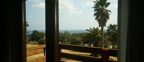 A wooden balcony with a view of palm trees and the ocean.