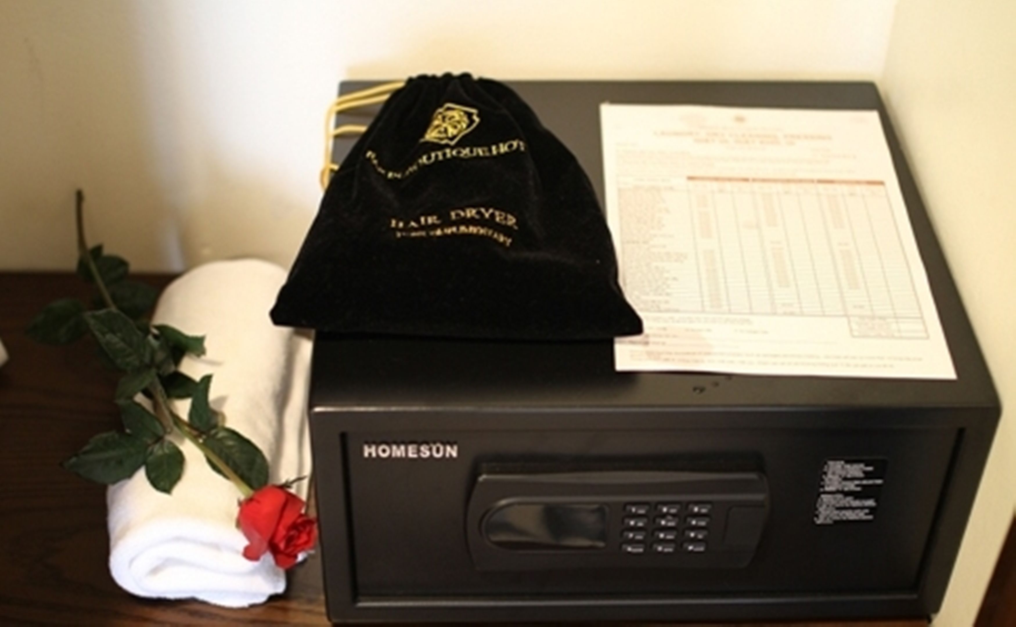 Um micro-ondas preto com etiqueta "HOMESUN", uma bolsa de veludo preta com um logotipo e uma rosa vermelha sobre uma toalha branca.