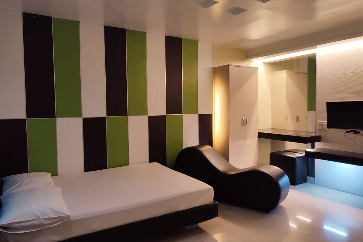 A modern hotel room with a bed, a chair, a desk, and a TV.