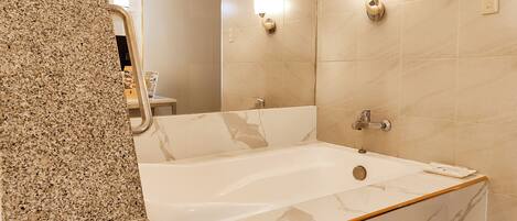 Un baño con bañera de mármol, encimera de granito y espejo.