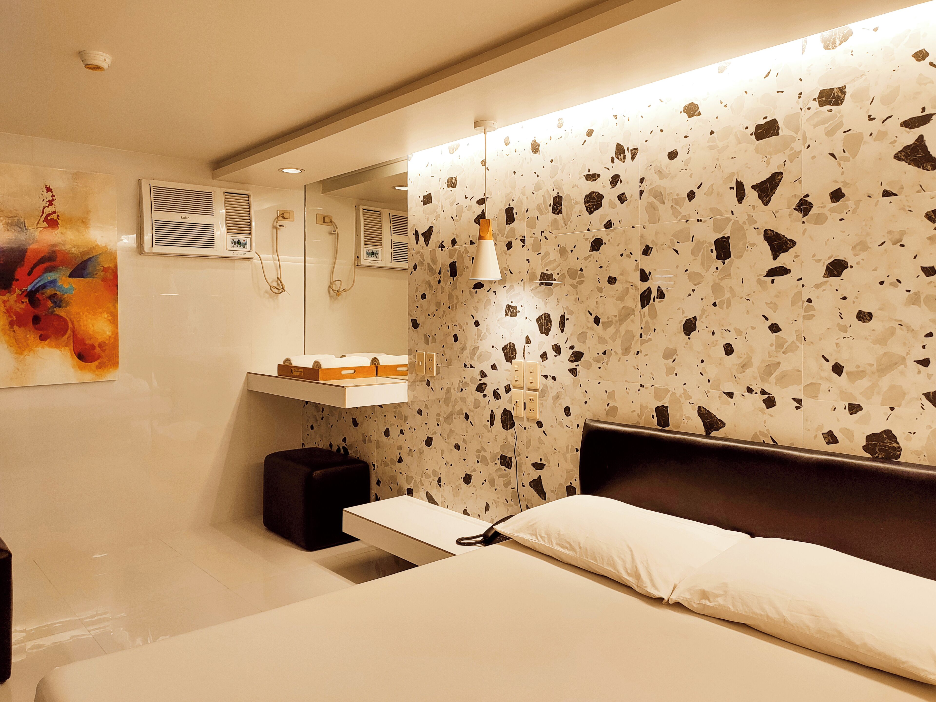 A modern bedroom with a bed, a nightstand, a mirror, and a wall with a unique terrazzo pattern.