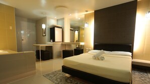 Una habitación de hotel moderna con una cama grande, una zona de estar separada, un baño y un espejo.