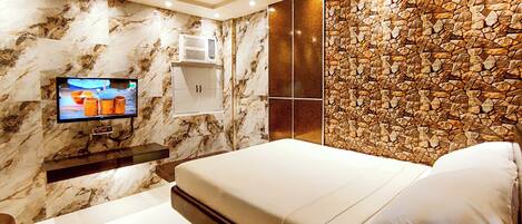 Un dormitorio moderno con pared de mármol, pared acento de piedra, televisor de pantalla plana, mesita de noche y cama con almohadas.