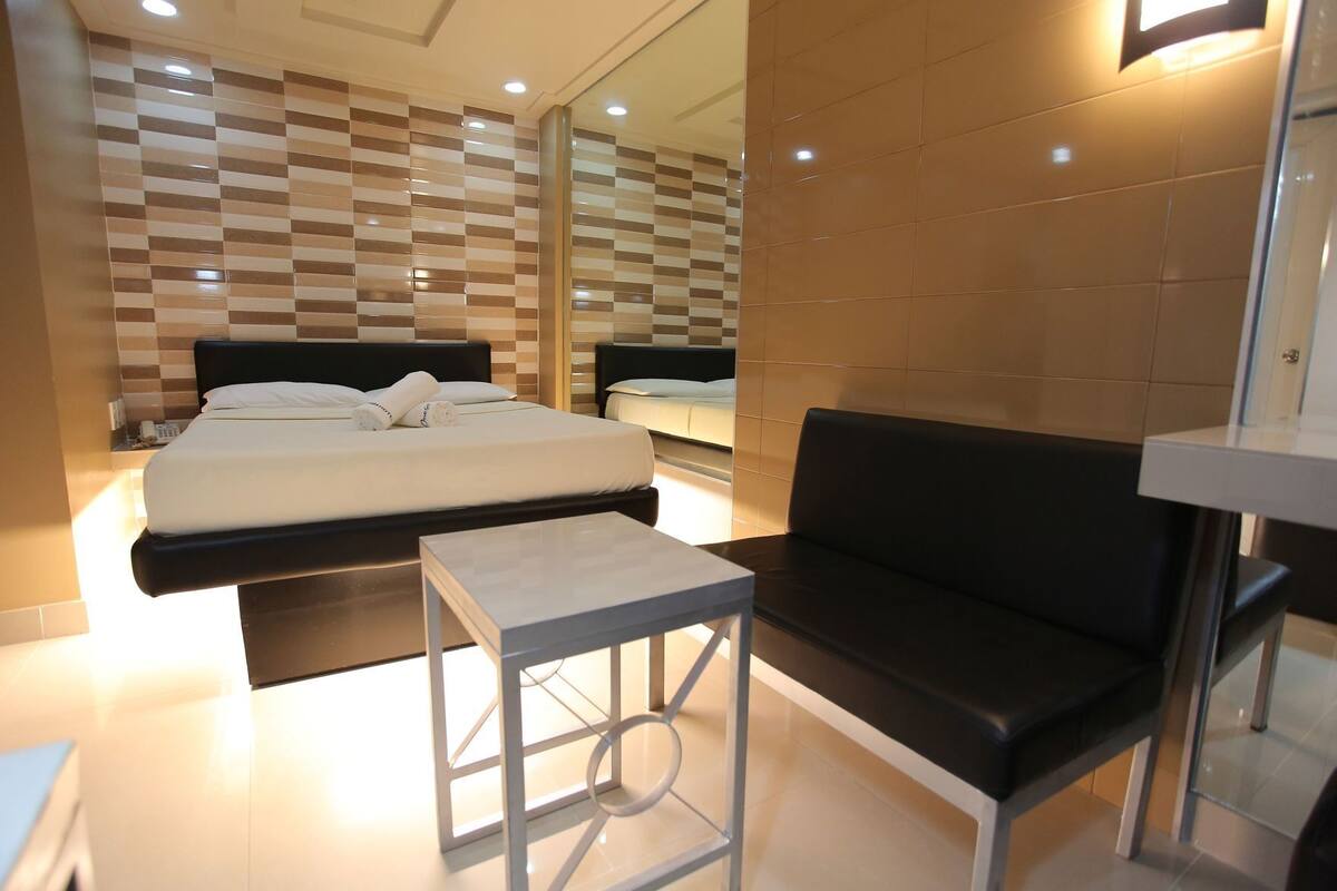 A modern hotel room with a large bed, a small table, a sofa, and a mirror.