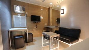 A modern room with a sofa, a small table, a TV, and a mirror. - One Serenata Hotel Bacoor (Bacoor City)
