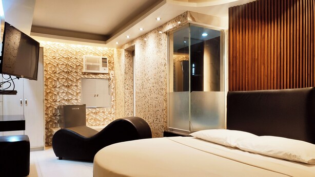 A modern hotel room with a large bed, a seating area, a television, and a wardrobe. - One Serenata Hotel Bacoor (Bacoor City)