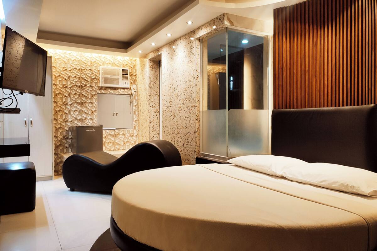 A modern hotel room with a large bed, a seating area, a television, and a wardrobe.