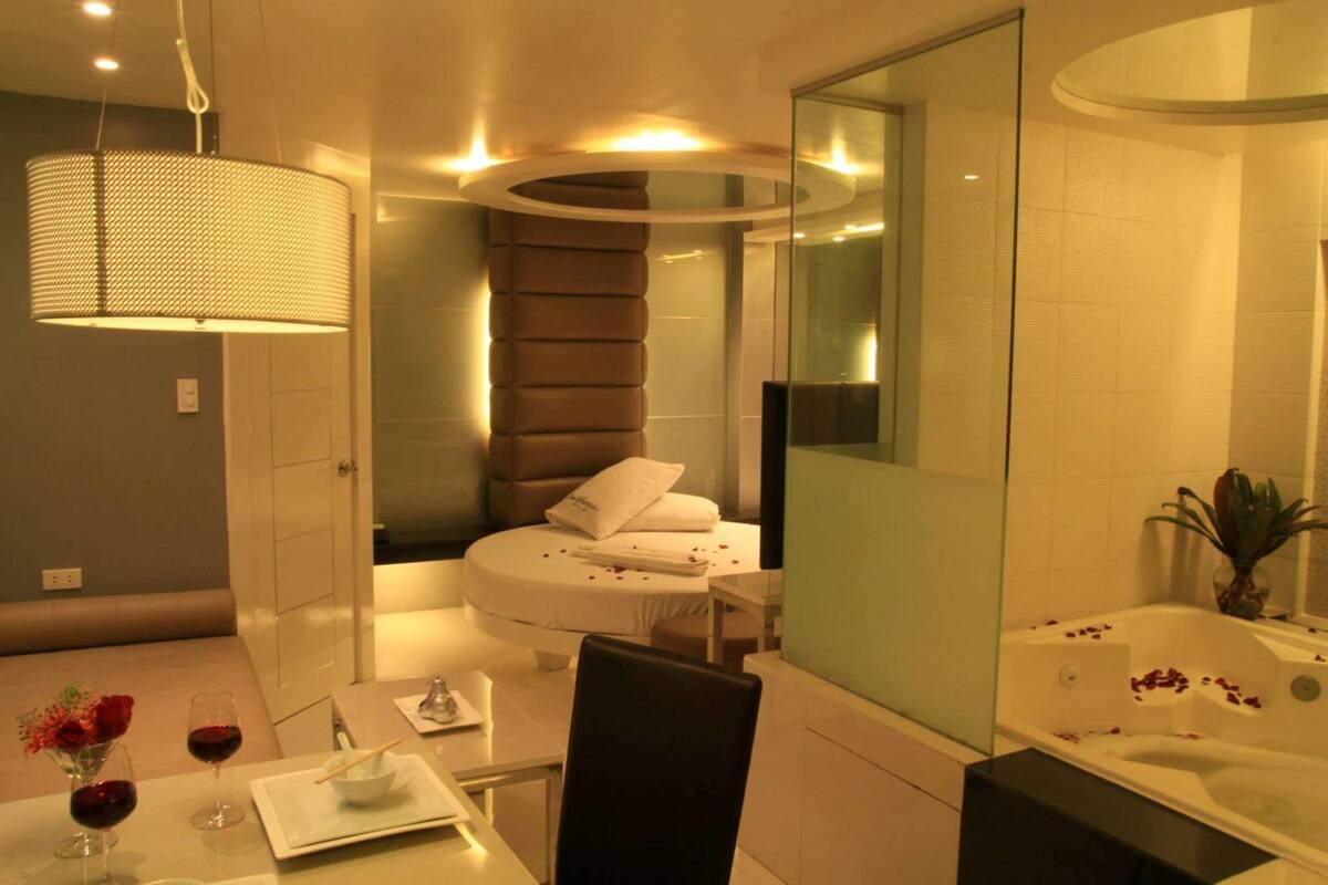 A modern bathroom with a bathtub, a round seating area, and a dining table with wine glasses and a flower arrangement.
