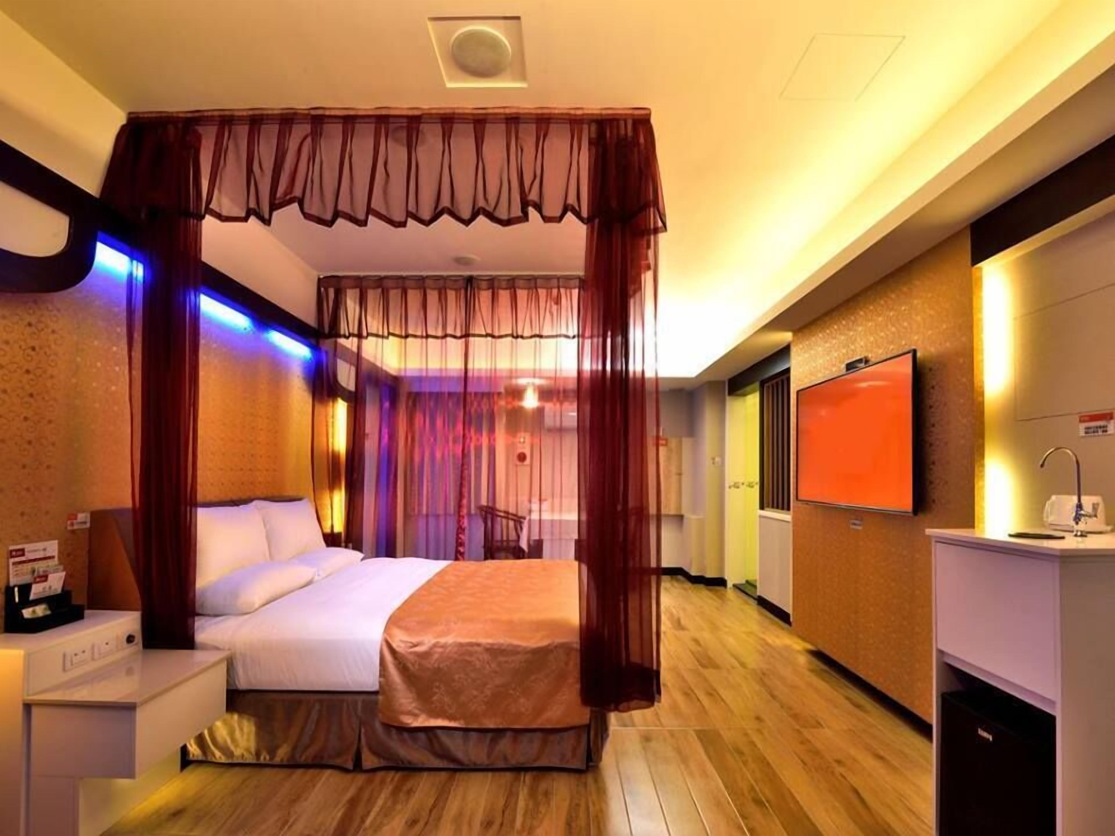 A hotel room with a bed, a bedside table, a TV, and a minibar.