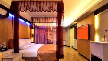 A hotel room with a bed, a bedside table, a TV, and a minibar.