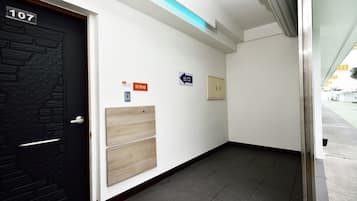 Pasillo con una puerta negra con el número 107, un interruptor de luz y un cartel que indica una salida.