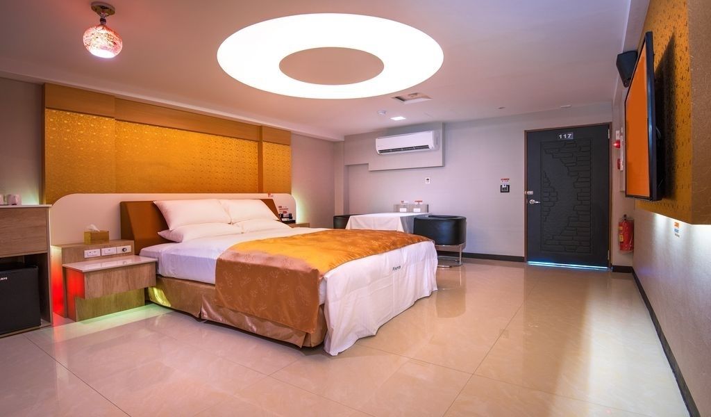 Une chambre d’hôtel moderne dotée d’un grand lit, de tables de chevet, d’un appareil de climatisation, d’un téléviseur à écran plat et d’une porte portant un numéro.