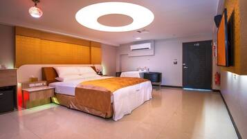 Une chambre d’hôtel moderne dotée d’un grand lit, de tables de chevet, d’un appareil de climatisation, d’un téléviseur à écran plat et d’une porte portant un numéro.