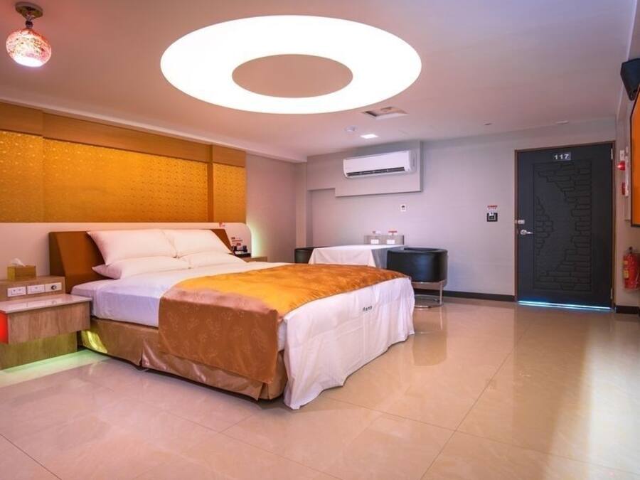 Une chambre d’hôtel moderne dotée d’un grand lit, de tables de chevet, d’un appareil de climatisation, d’un téléviseur à écran plat et d’une porte portant un numéro.