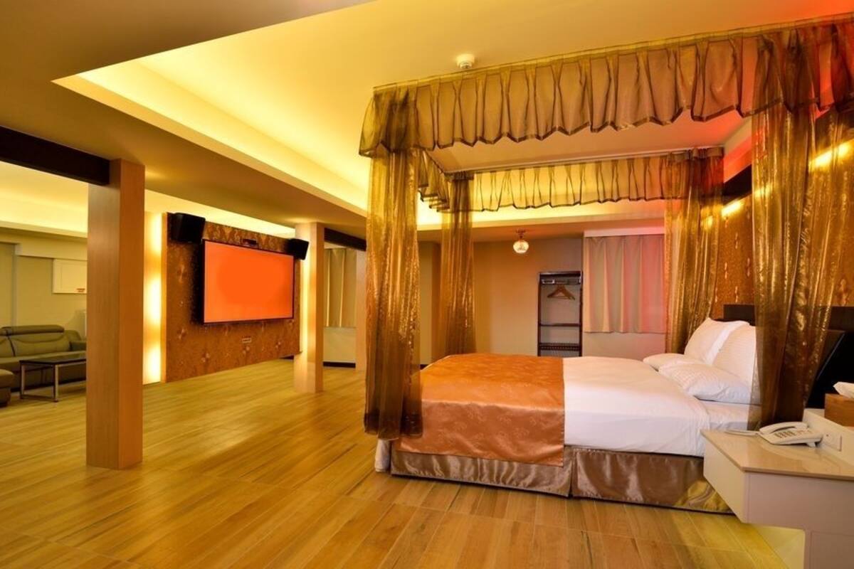 Ruime hotelkamer met een groot bed, een televisie en een zithoek met een bank en een tafel.