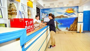 A reception area with a counter, a red tip box, and a mural of a coastal scene. - Dreamwave Hotel Puerto Galera (Puerto Galera)