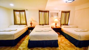 A hotel room with four single beds, each with a pillow and a folded towel. There are two bedside tables with lamps. The room has a carpeted floor and a window with curtains. - Dreamwave Hotel Puerto Galera (Puerto Galera)