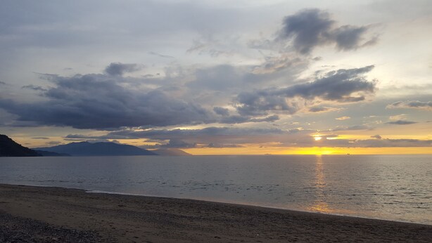 A beach with a sunset over the ocean, featuring a calm sea and a distant mountain range. - Dreamwave Hotel Puerto Galera (Puerto Galera)
