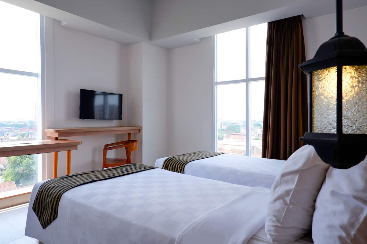 Ein Hotelzimmer mit zwei Betten, einem Schreibtisch, einem Fernseher und einem großen Fenster mit Blick.