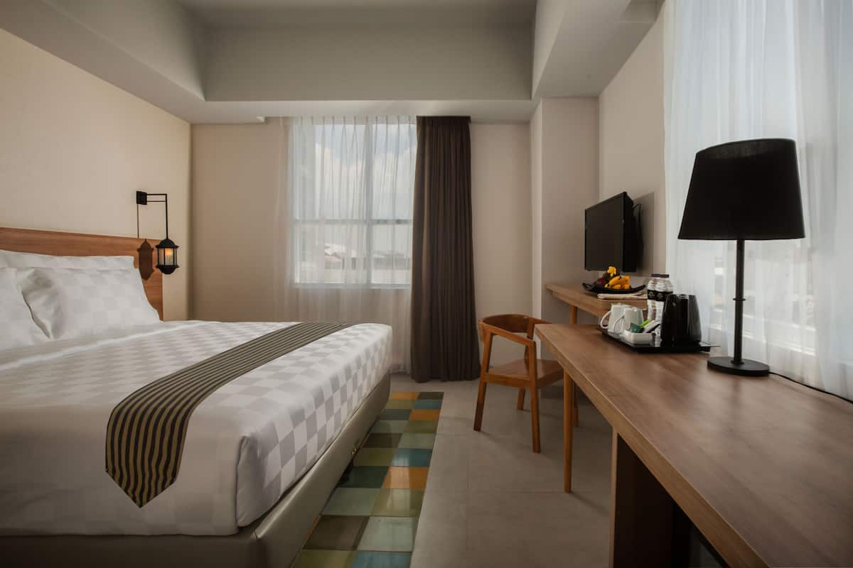 Ein Hotelzimmer mit Bett, Schreibtisch, Stuhl, Fernseher und einem fensterbepflanzten Fenster.