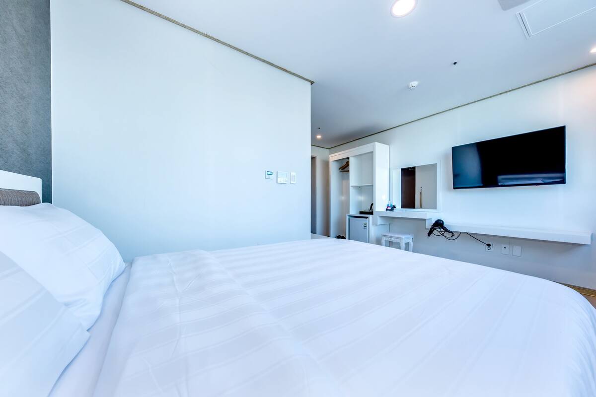 Ein modernes Hotelzimmer mit einem großen Bett, einem flachbildfernseher an der Wand und einem begehbaren Kleiderschrank.