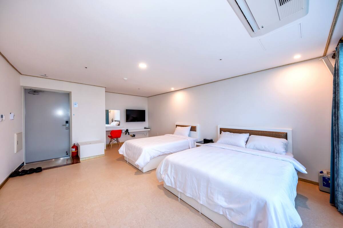 Ein Hotelzimmer mit zwei Betten, einem Fernseher, einem Schreibtisch und einem roten Sessel.