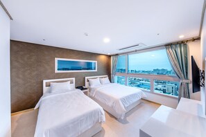Ein Hotelzimmer mit zwei Betten, einem großen Fenster mit Blick auf die Stadt, einem Wand-Fernseher und einem Flachbildfernseher an der Wand.