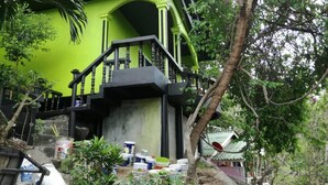 Une maison verte avec un escalier menant à un balcon. On y voit des matériaux de construction et des outils éparpillés.
