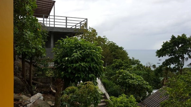 Un immeuble doté d’un balcon donnant sur un jardin luxuriant et la mer.