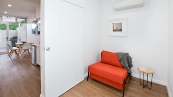 A modern interior with a wooden floor, a red sofa, a small table, and a kitchen area in the background.