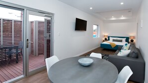 A modern living room with a round table, white chairs, a grey sofa, and a bed with a blue headboard. - Loxton Courthouse Apartments (Loxton)