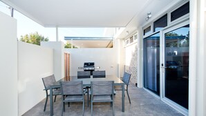 A patio with a table and chairs, a grill, and a sliding glass door. - Loxton Courthouse Apartments (Loxton)