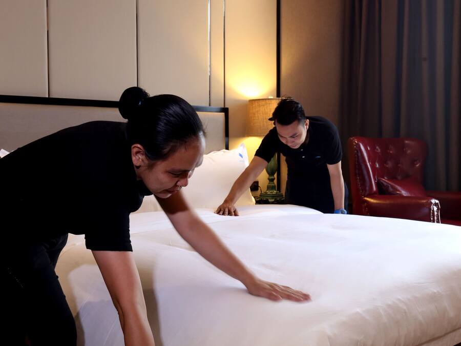 Una habitación de hotel con una cama bien hecha, un sillón de cuero rojo y una lámpara en la mesita de noche.