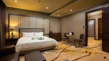 A hotel room with a large bed, a desk with a chair, a small table with a chair, and a bathroom visible through an open door.
