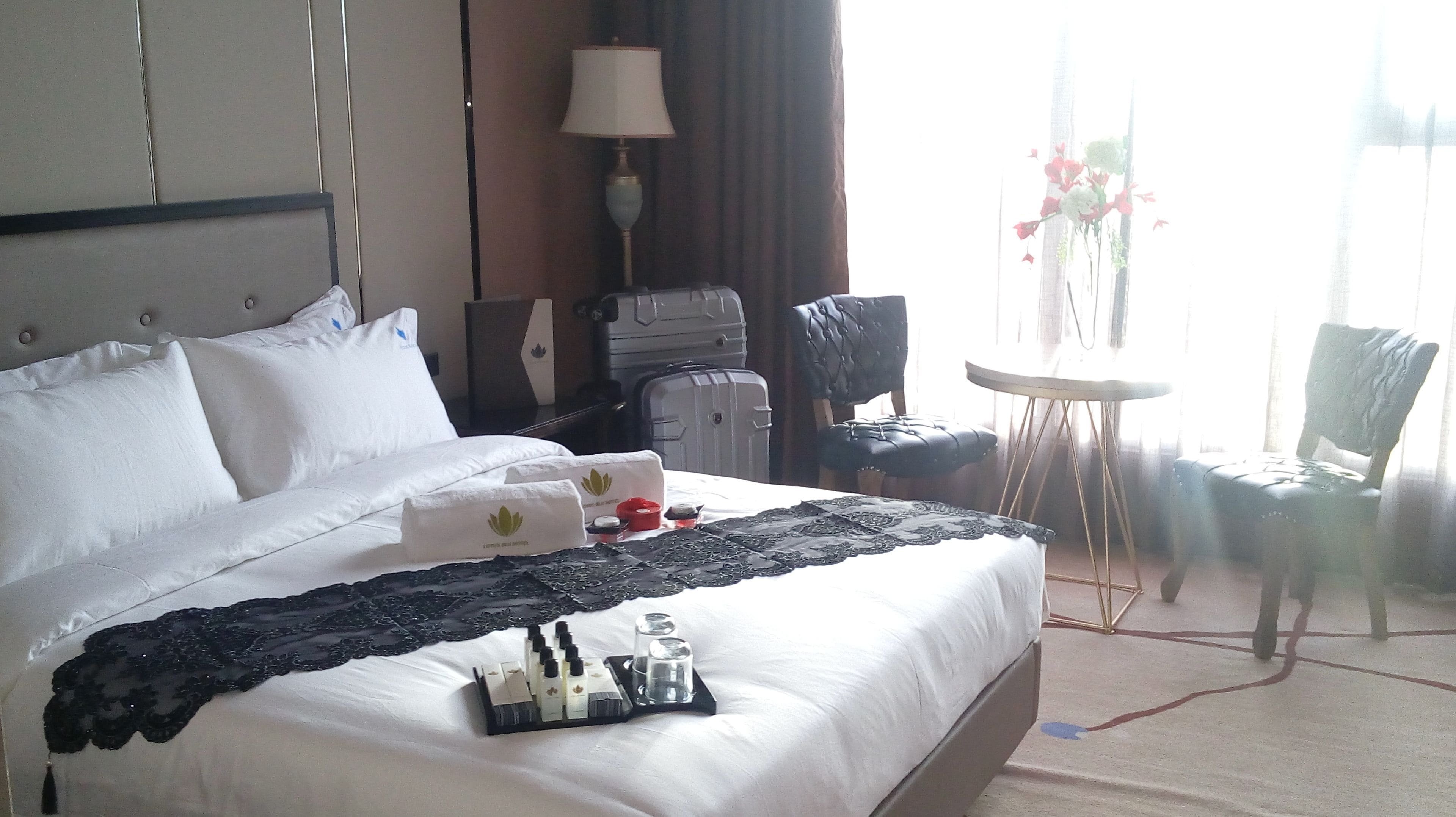 A hotel room with a large bed, a desk, a chair, a small table, and a lamp.