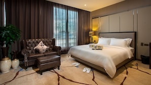 Habitación de hotel moderna con una cama grande, un sofá de cuero, una planta en maceta y vistas al exterior.