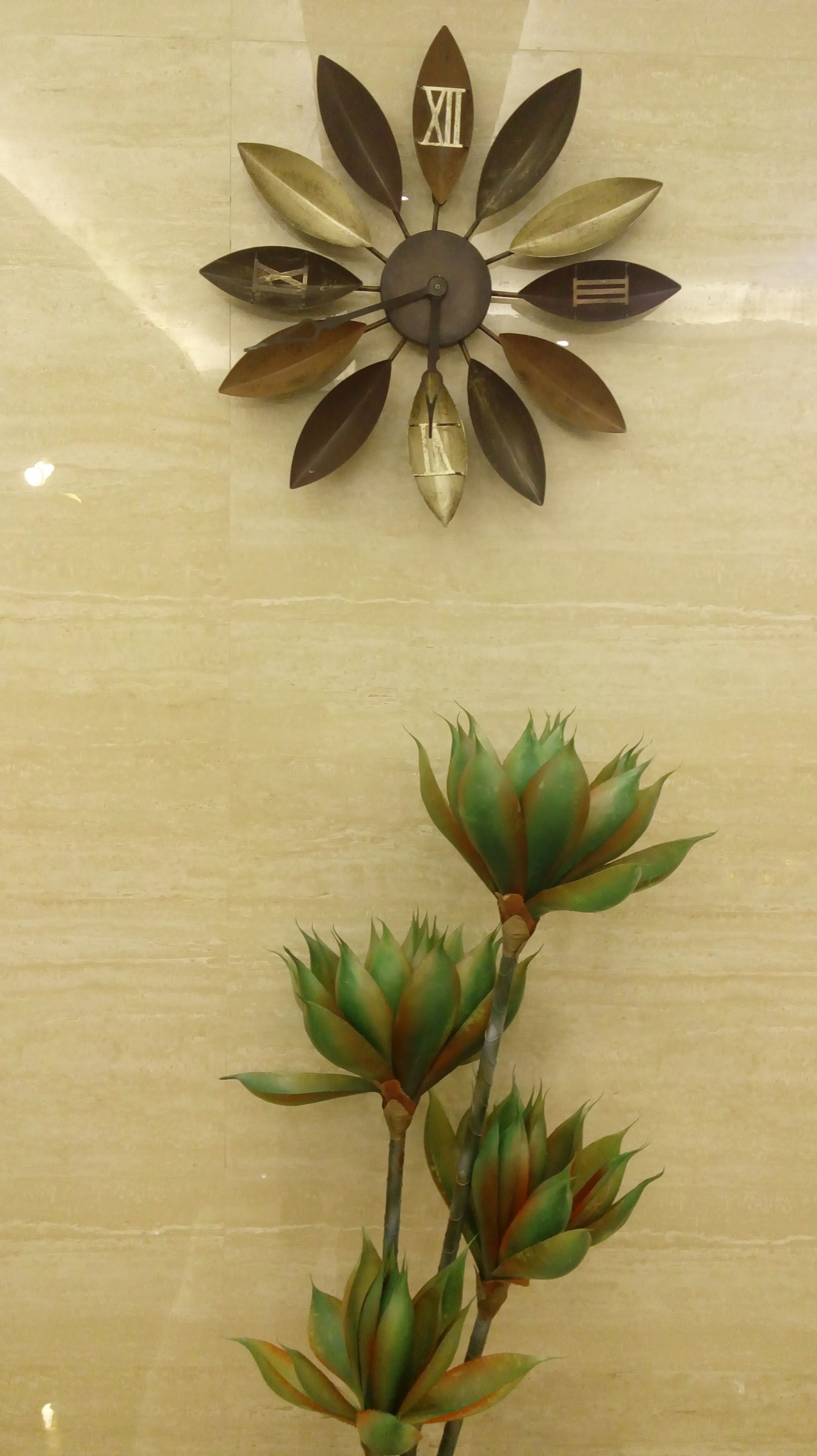 Une horloge murale avec les chiffres romains, le XII en particulier, et une composition florale décorative placée en dessous.