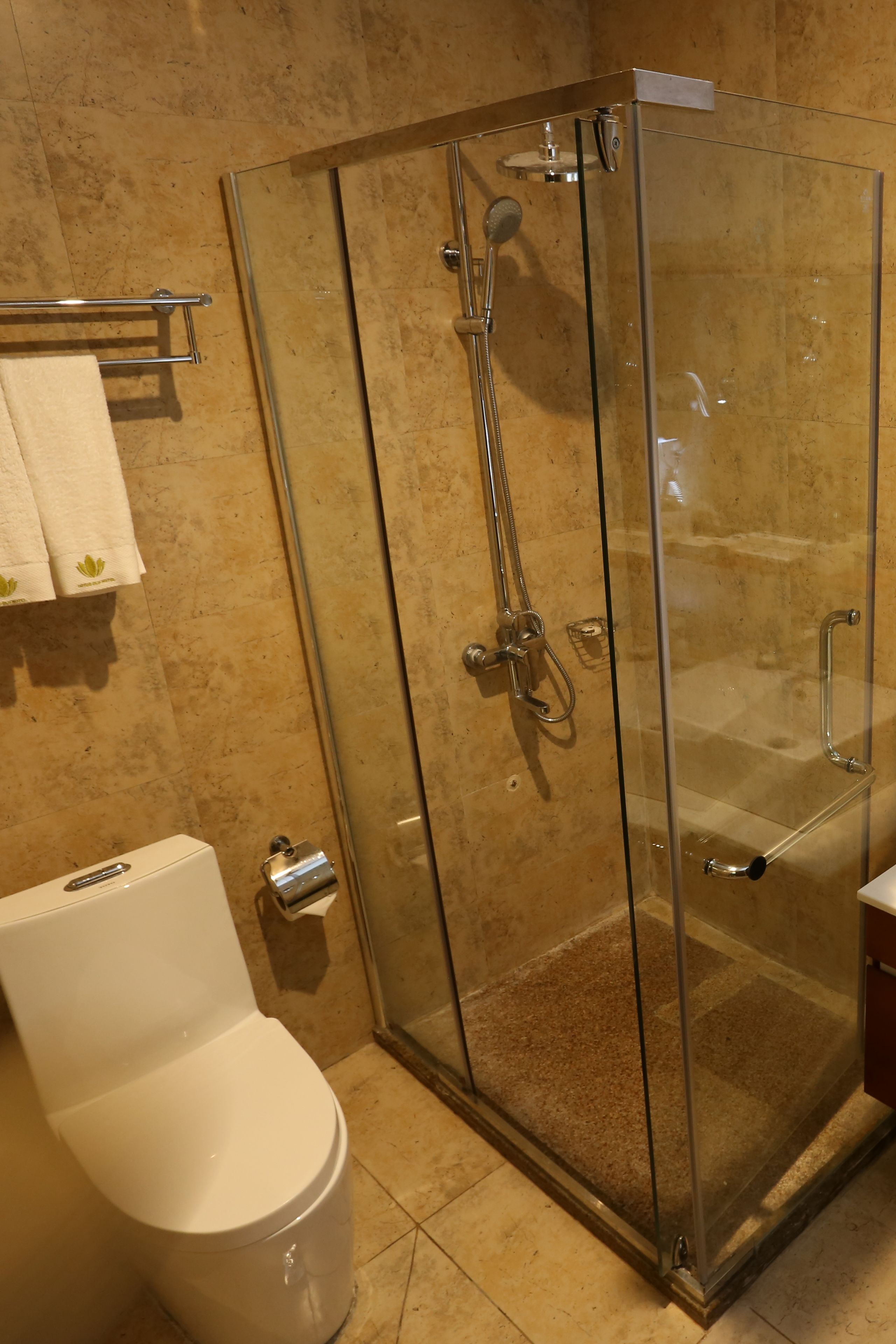 Un baño moderno con ducha de vidrio, inodoro y toallero con toallas blancas.