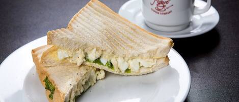 A sandwich on a plate with a cup of coffee in the background.