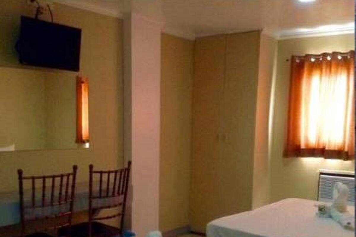 A room with two beds, a TV mounted on the wall, a chair, and a window with curtains.
