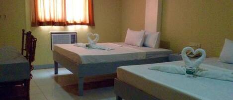 A hotel room with two single beds, a chair, a table, and a window with curtains.