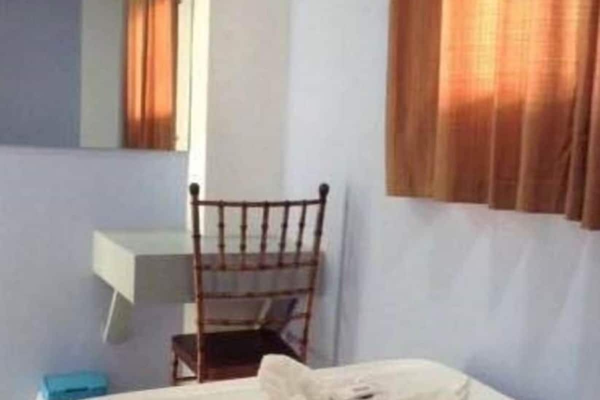 A hotel room with a bed, a chair, a desk, and a window with curtains.